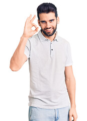 Young handsome man with beard wearing casual polo smiling positive doing ok sign with hand and fingers. successful expression.