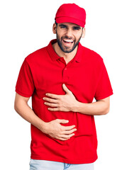Young handsome man with beard wearing delivery uniform smiling and laughing hard out loud because funny crazy joke with hands on body.