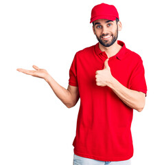 Young handsome man with beard wearing delivery uniform showing palm hand and doing ok gesture with thumbs up, smiling happy and cheerful
