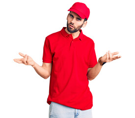 Young handsome man with beard wearing delivery uniform clueless and confused with open arms, no...