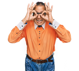 Middle age indian man wearing casual clothes and glasses doing ok gesture like binoculars sticking tongue out, eyes looking through fingers. crazy expression.