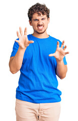 Young handsome man with curly hair wearing casual clothes smiling funny doing claw gesture as cat,...