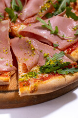 Pizza with ham, arugula and pistachios served on wooden platter