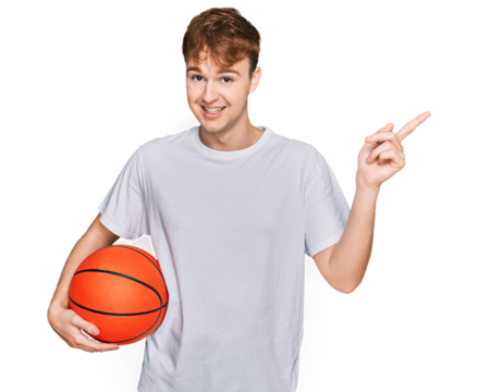 Young caucasian man holding basketball ball smiling happy pointing with hand and finger to the side
