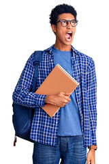 Young african american man wearing student backpack holding book angry and mad screaming frustrated and furious, shouting with anger. rage and aggressive concept.