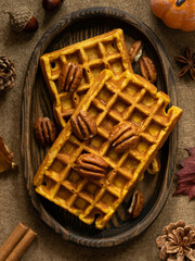 Top view of pumpkin waffles with pecan nuts and maple syryp served on a oval wooden plate. Autumn pastry. Brown background