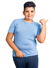 Little boy kid wearing sports workout clothes smiling with happy face looking and pointing to the side with thumb up.