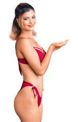 Young beautiful woman wearing bikini pointing aside with hands open palms showing copy space, presenting advertisement smiling excited happy