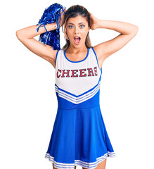 Young beautiful woman wearing cheerleader uniform crazy and scared with hands on head, afraid and...