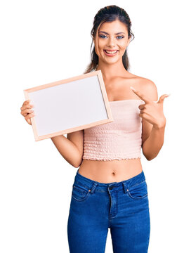 Young beautiful woman holding empty white chalkboard smiling happy pointing with hand and finger