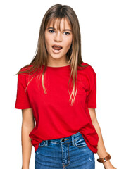 Fototapeta premium Teenager caucasian girl wearing casual red t shirt in shock face, looking skeptical and sarcastic, surprised with open mouth