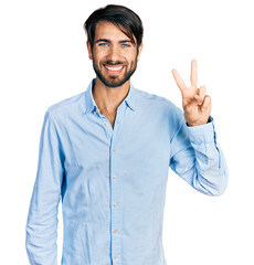 Hispanic man with blue eyes wearing business shirt showing and pointing up with fingers number two while smiling confident and happy.