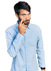 Hispanic man with blue eyes wearing business shirt pointing to the eye watching you gesture, suspicious expression