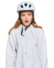 Beautiful young caucasian girl wearing bike helmet scared and amazed with open mouth for surprise, disbelief face