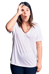 Obraz na płótnie Canvas Young beautiful brunette woman wearing casual t-shirt doing ok gesture shocked with surprised face, eye looking through fingers. unbelieving expression.
