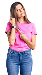 Beautiful caucasian woman wearing casual clothes in hurry pointing to watch time, impatience, looking at the camera with relaxed expression