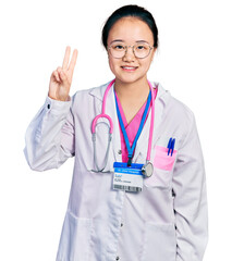 Young chinese woman wearing doctor uniform and stethoscope showing and pointing up with fingers number two while smiling confident and happy.
