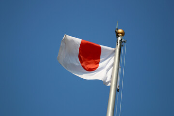 National flag of Japan flaps in the wind. Bright blue sky background.
