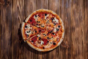 Tomato-based pizza with mozzarella cheese, hunting sausages, salami, olives, mushroom sauce. On a wooden background