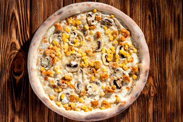 Appetizing pizza on a creamy sauce with mushrooms, corn, chicken fillet and mozzarella cheese on woden background