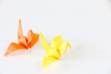 Orange Japanese origami paper crane follows yellow one, on white background