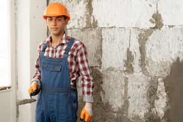 Arabic man master plasters the walls, portrait of builder in hard hat making repairs in the...