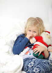 Fototapeta premium Cute little girl is very surprised and excited, lying on white background and holding little santa claus, looking straight. Christmas holiday