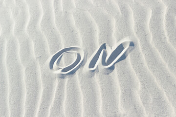 ON written with a finger on the white sand. concept turn on or open, word on sand