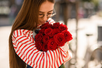 Close-up view bouquet of red rose which tenderly holding young woman and look at it