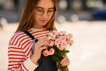 Close-up portrait of pretty young woman with bouquet of fresh light pink roses in her hand