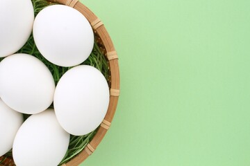 Fresh white chicken eggs in wooden rattan wicker basket on green background. Natural healthy nutrition organic farm food product concept. World egg day, easter holiday composition. Close-up, flatlay