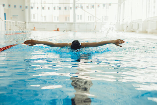 Professional sportswoman in cap swimming in pool and performing Butterfly stroke while competing in pool during race 