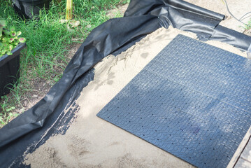 Walkway installation near a weather wooden deck with polypropylene paver base panel, leveling sands and landscape fabric in garden