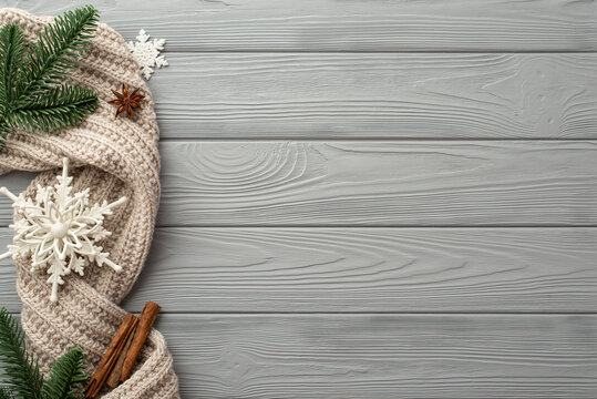 Winter holidays concept. Top view photo of snowflakes knitted scarf pine branches anise and cinnamon sticks on grey wooden desk background with copyspace