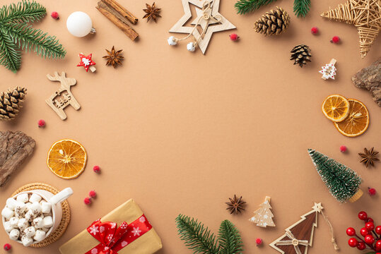 Top view photo of christmas decorations wood ornaments cup of cocoa pine cones branches bark giftbox mistletoe cinnamon dried orange slices on isolated beige background with empty space in the middle