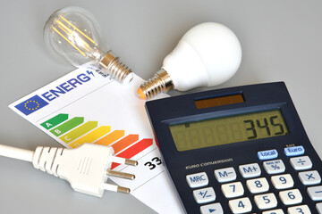 nergy efficiency rating table with light bulbs, calculator and powercord on grey background,...