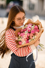 Selective focus on bouquet of pink rose which tenderly holding young woman and look at it