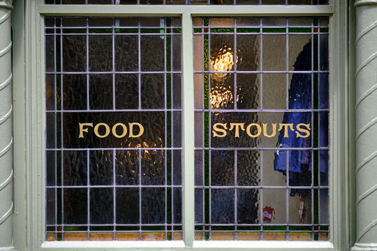 Close-up of a window of a traditional British pub. It reads: Food, Stouts.