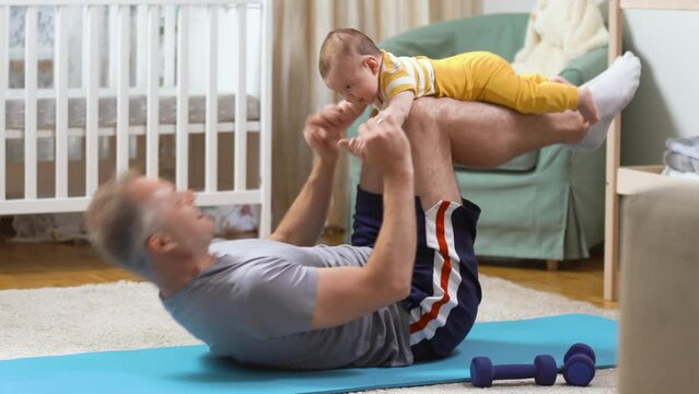 Middle-age father doing sports exercises together with his baby in the nursery. Sport, family life and active lifestyle.