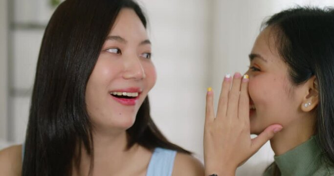 Gen Z asia people gay LGBT girl friend tell fun good news at ear happy overjoy. Open mouth amazed shock face in young adult asian couple lady listen black Friday sale rumor gossip laugh smile at home.
