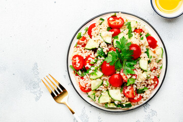 Bulgur tabbouleh salad with fresh tomatoes, cucumbers and parsley. Traditional Middle Eastern and Arabic dish. White kitchen table background, top view