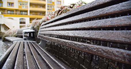 Frozen city bench in the ice icicles. Climatic icing.   Icy city bench after winter natural disaster. City environment in a winter..