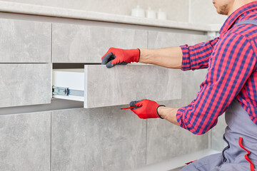 Repairman Repairing Cabinet Hinge In Kitchen. Help for People in New House. Male hand adjusting a...
