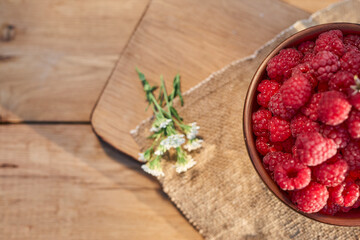 Plate of fresh ripe raspberries on wooden table in a garden. Harvested red raspberries in dishes. Summer fruit for healthy diet.