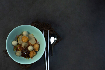 Dried yellow noodles in a green cup There are white chopsticks on the side. and silver spoon on a blurry dark gray background