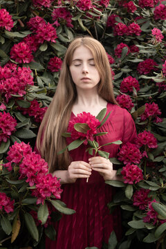 art portrait in nature of blonde woman hiding in rhododendron bush holding pink flower