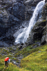 A man is going up to mountains with unfocused waterfall and rocks as background. Travel scene in mountains