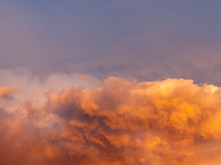 Colorful orange thunderstorm clouds at sunset time. Close-up of a beautiful cloudscape in the nature. Natural weather phenomenon in the sky. Abstract background of a dramatic sky.