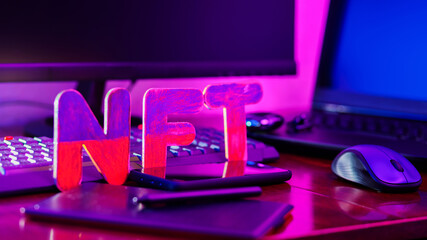 NFT creation by a digital artist in a home office. NFT lettering at workplace with graphics tablet, pen, smartphone and computer equipment. Crypto art concept in neon light