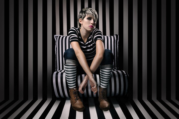 beautiful mexican model poses elegant and sensual for artsy portrait with stripes in black and white while sit on striped chair in front of stripe pattern wall background with black and white socks